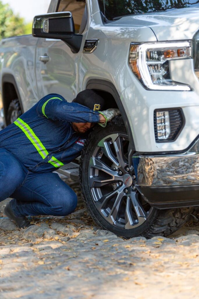 Mechanic working on the wheel of a white off-road vehicle outdoors, fixing a problem.