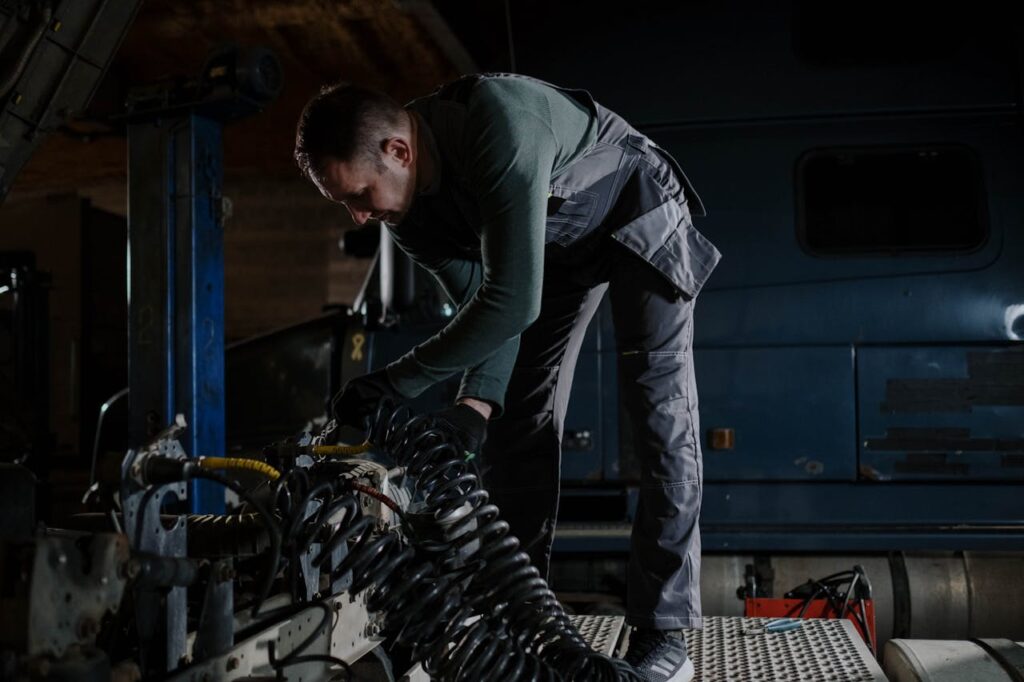 Mechanic fixing truck components indoors at an automotive repair shop.